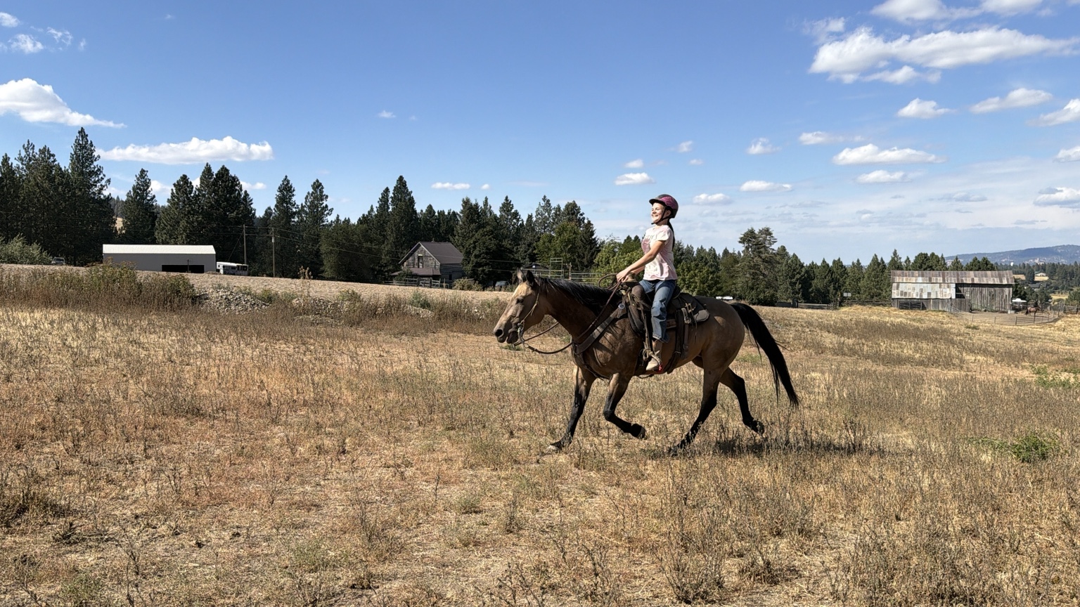 Student riding a ranch horse in the open field at Stache Ranch